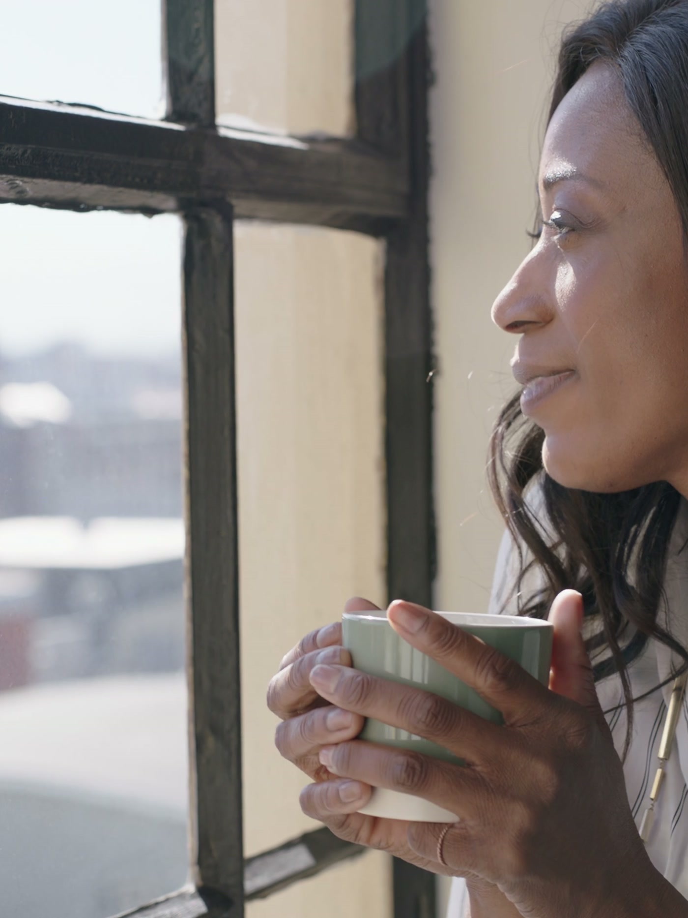 Woman at home by a window, holding a mug of tea